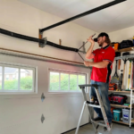 Professional garage door technician in black uniform inspecting torsion springs above a white residential garage door in Minnesota